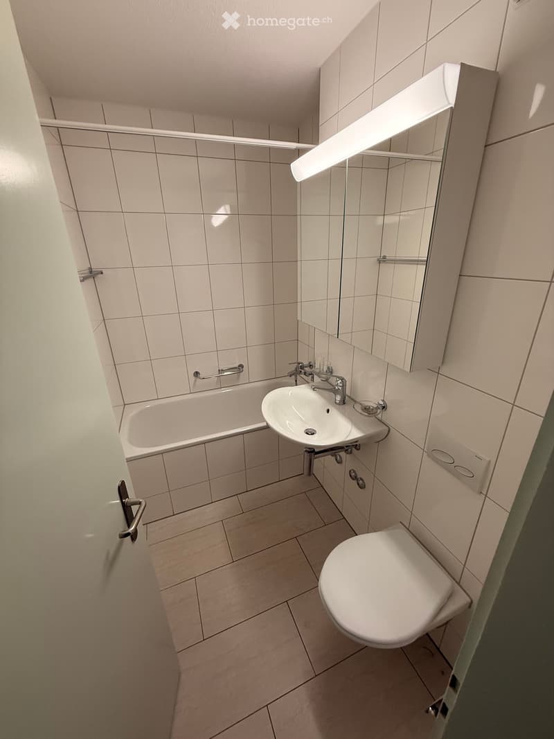 Modern bathroom with white tiled walls, a bathtub, a sink, a toilet, and a mirrored cabinet with built-in lighting.