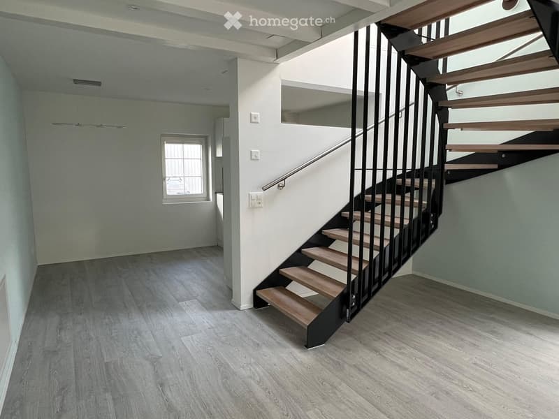 Modern hallway with wooden flooring, a staircase with wooden steps and metal railing, and a window providing natural light.