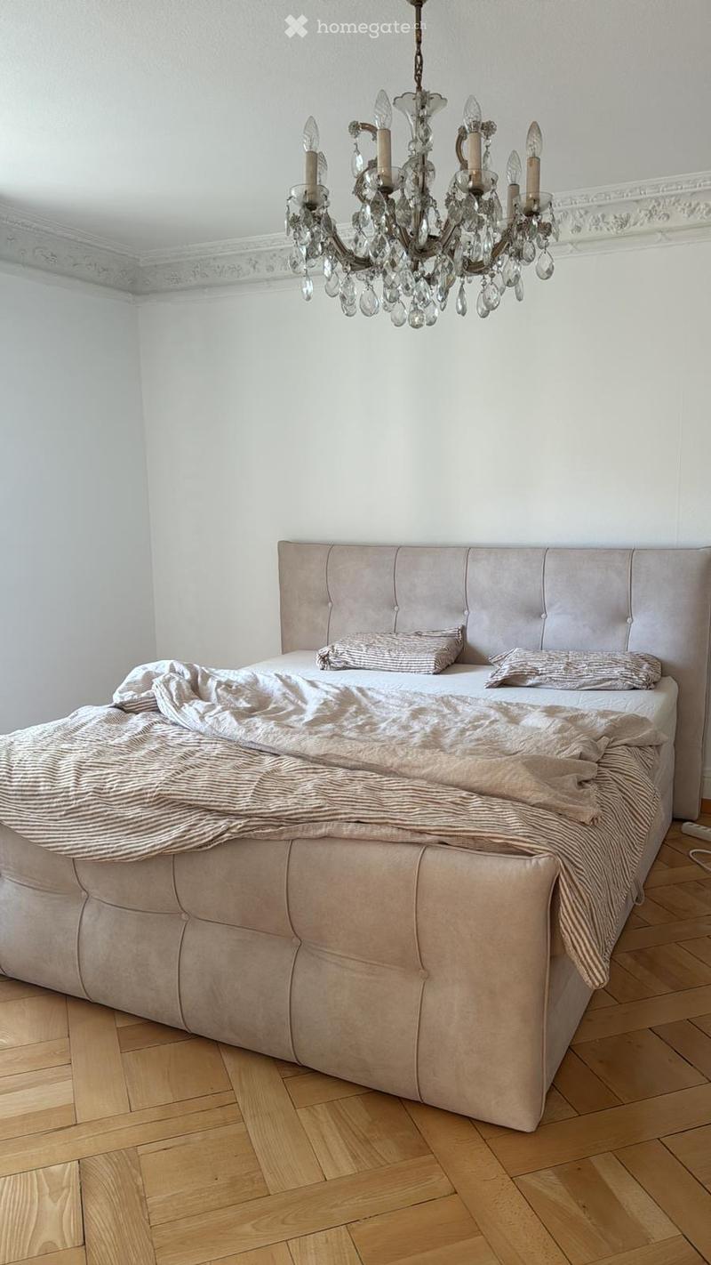 A bedroom with a tufted headboard bed, a chandelier, and pillows on the bed.