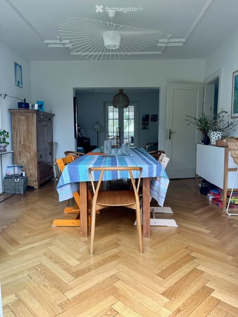Dining room with herringbone wooden flooring, a round dining table with chairs, a modern fan light fixture, and a wooden cabinet.