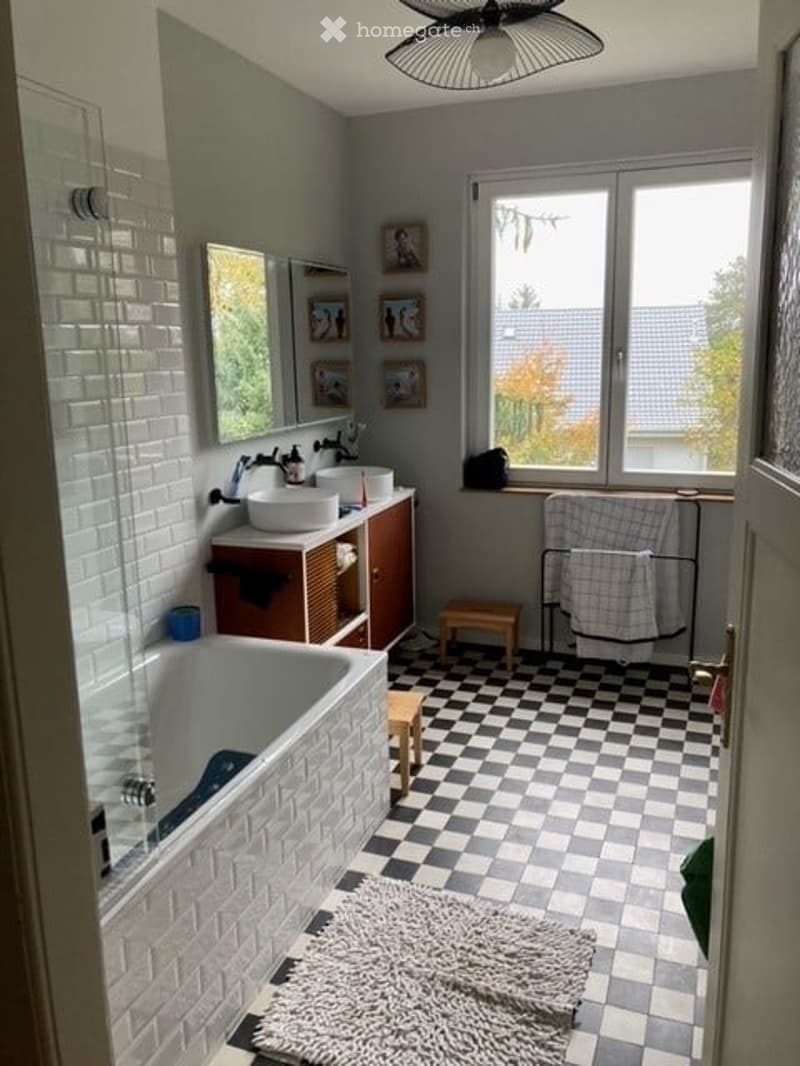 Bathroom with white brick walls, checkered floor, bathtub, sink, mirror, and small wooden stool.