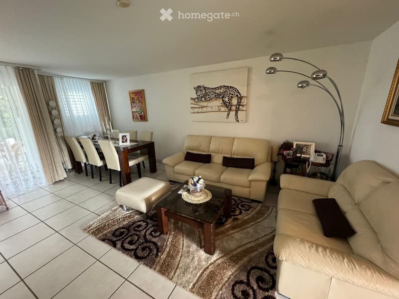 Living room with beige sofas, coffee table, ottoman, dining area, and artwork on the walls.
