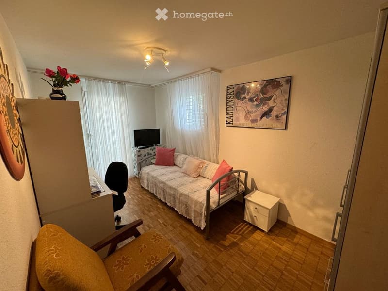 A small, furnished room with a sofa, chair, table, screen, vase, and picture on the wall.