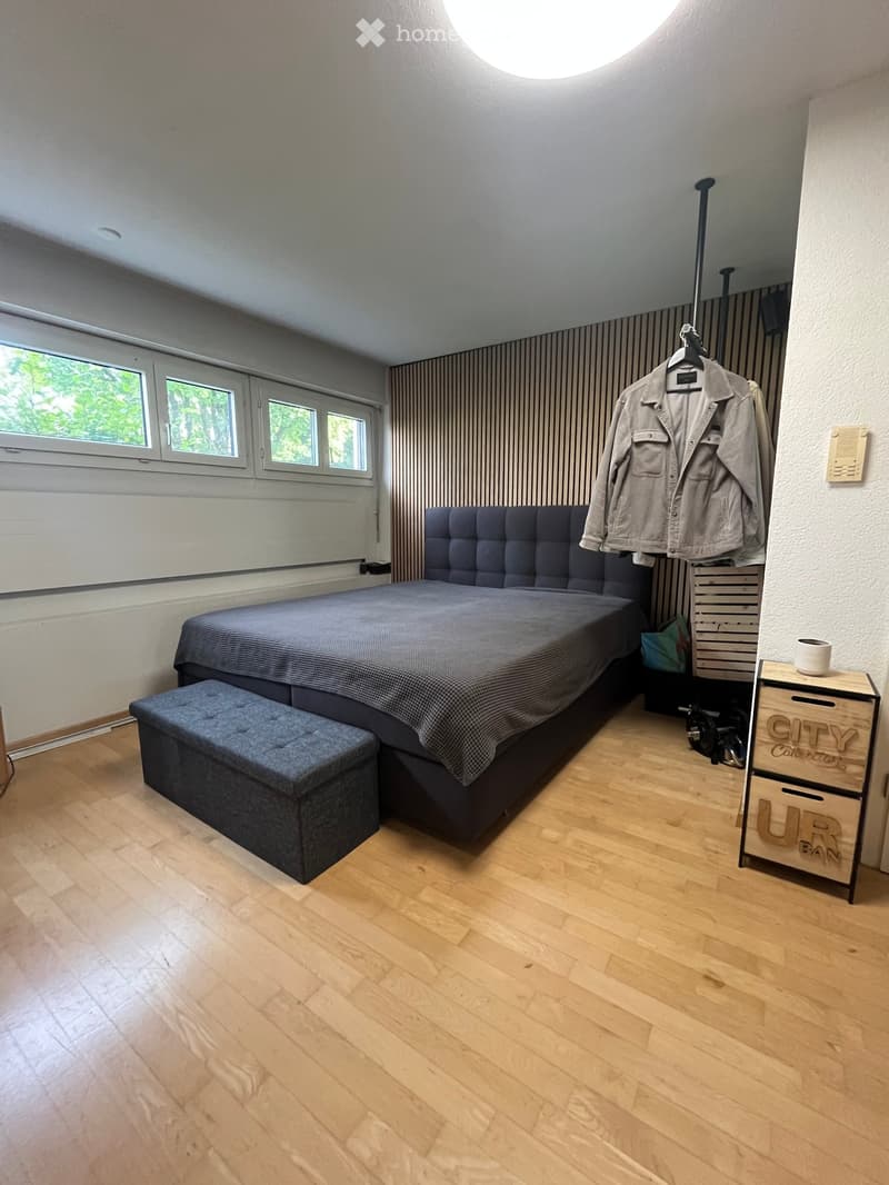 Modern bedroom with wooden flooring, large bed with dark blue bedding, matching stool, wardrobe, and small wooden cabinet.