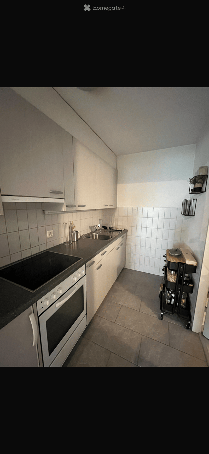 Modern kitchen with white cabinets, black countertop, built-in oven, sink, and small cart with storage compartments.