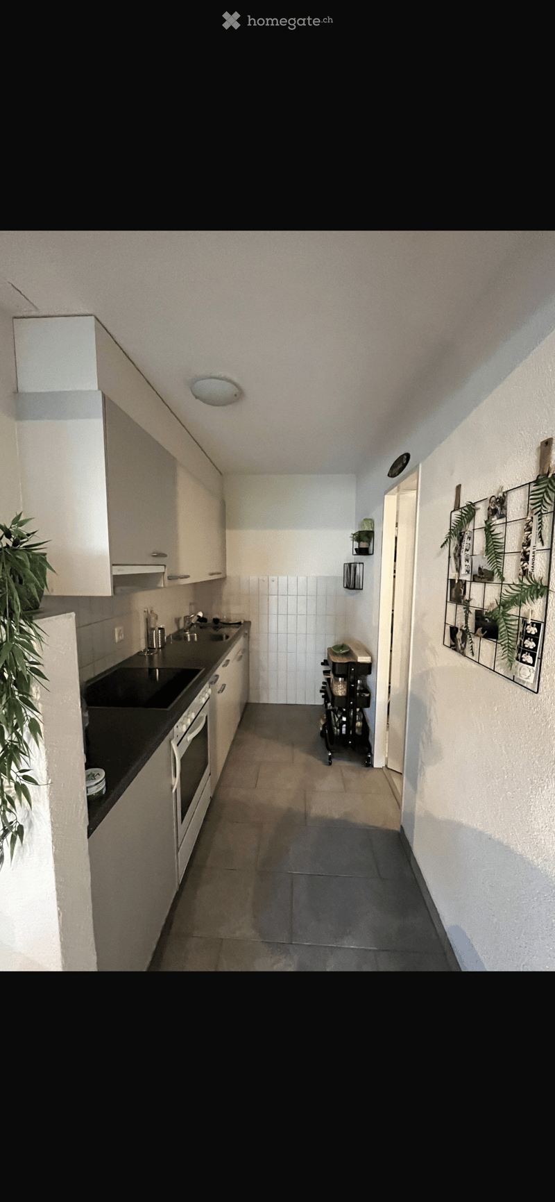 Modern kitchen with white cabinets, black countertops, a sink, an oven, and a small cart. The walls are tiled, and there is a plant on the counter and framed pictures on the wall.