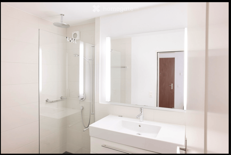 Modern bathroom with white tiles, a large mirror, a sink with a modern faucet, and a glass-enclosed shower with a handheld showerhead.