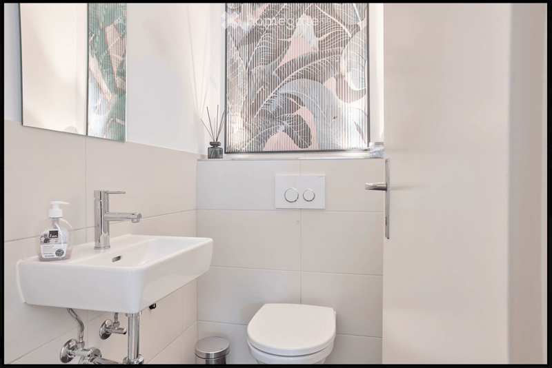 Modern bathroom with white tiles, a white sink with a chrome faucet, a toilet, a mirror, and a soap dispenser on the sink.