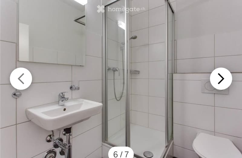 Modern bathroom with white tiles, a glass-enclosed shower, a sink with a mirror, and a toilet.