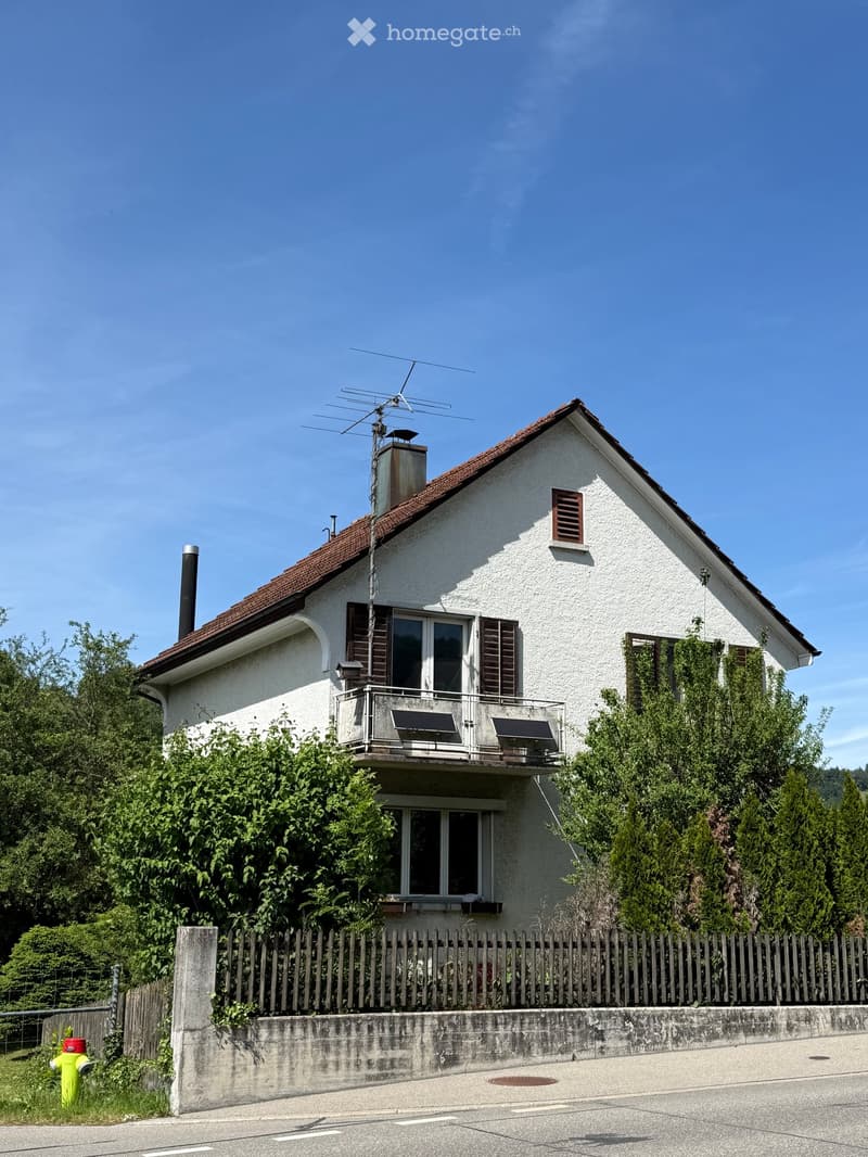Two-story house with white exterior, red-tiled roof, multiple windows, and a balcony on the upper level.