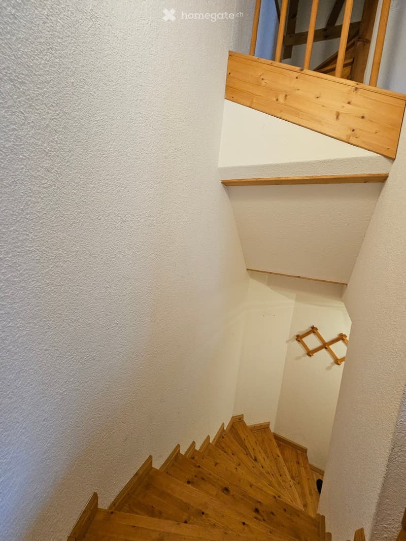 Wooden staircase with white walls and wooden railings, leading upwards.