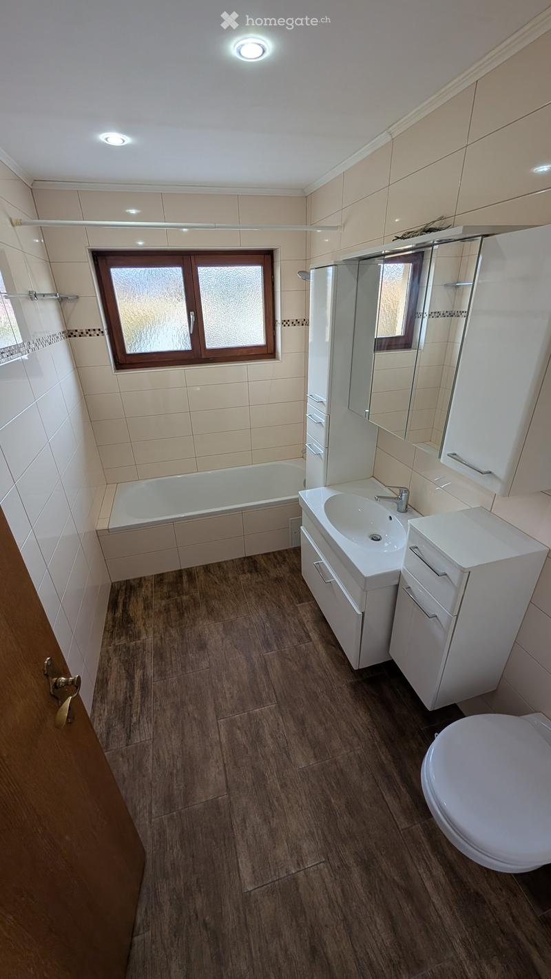 Bathroom with tile flooring, white bathtub, white sink with mirror cabinet, and toilet.