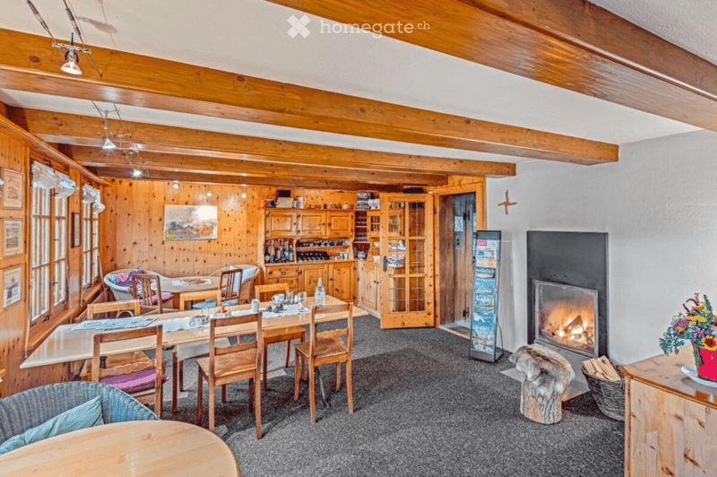Cozy living and dining area with wooden beams, a dining table with chairs, a fireplace, a cabinet, and a refrigerator.