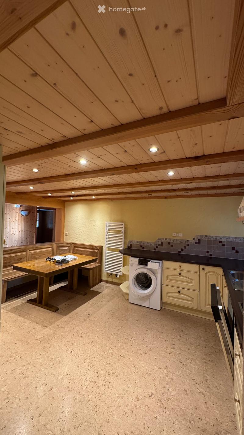 Cozy attic room with wooden beams, a table with benches, a washing machine, and built-in cabinets.