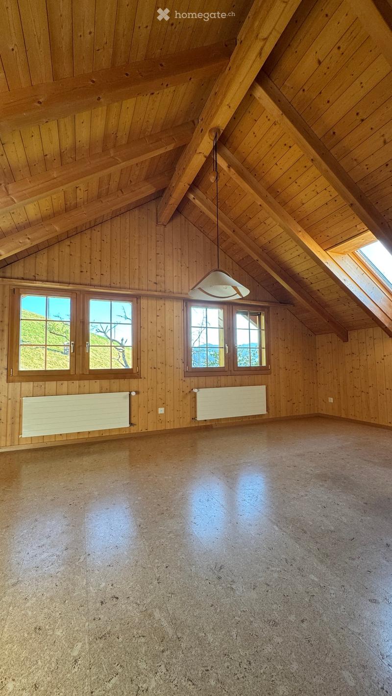 Empty attic space with wooden walls and ceiling, large windows, and a hanging light fixture.