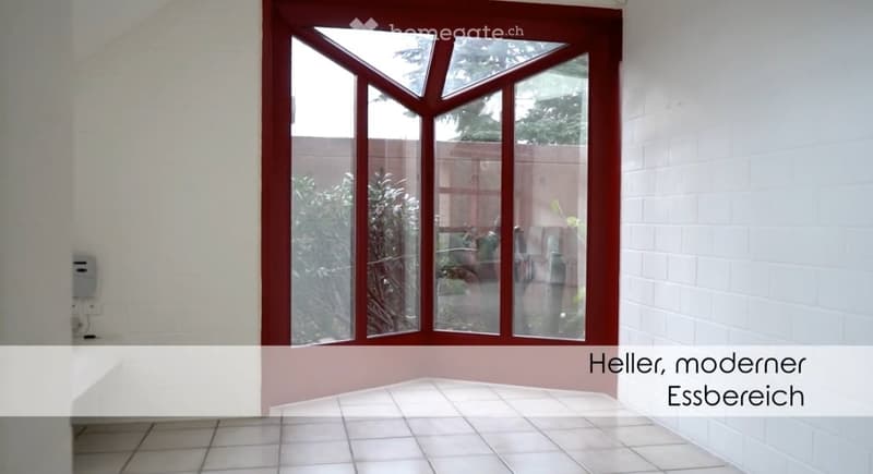 Empty dining area with white tiled floor, white brick walls, and a large, multi-paned window with red framing, offering a view of an outdoor space.