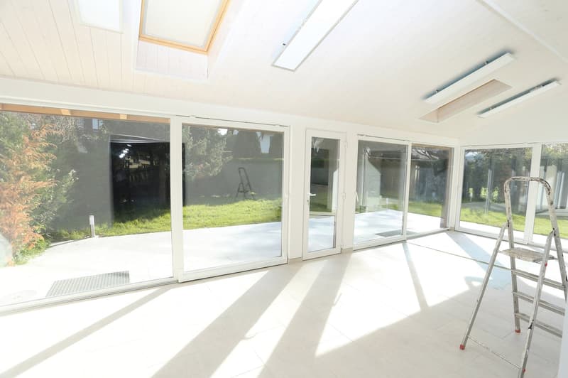 Unfurnished Room. An empty room with white tiled flooring, large glass doors, and white walls. There are three ceiling lights and a ladder in the corner.