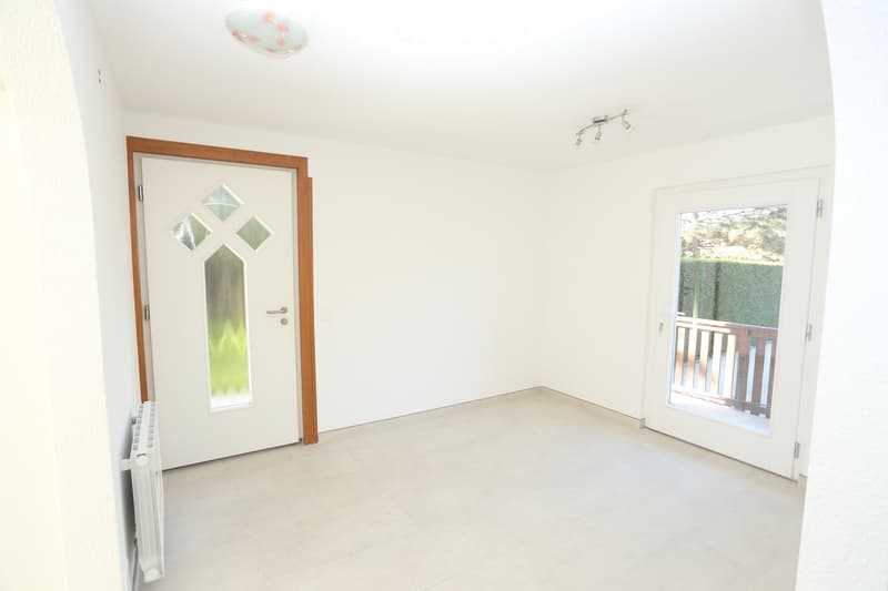 Unfurnished Room. An empty room with white walls, tiled floor, and two doors. One door has a glass panel, and the other leads to a balcony with a wooden railing. A ceiling lamp and a white radiator are also present.