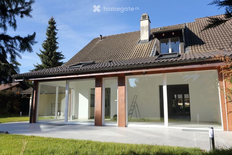 House. Modern house with brown tiled roof, large glass windows, and a patio.