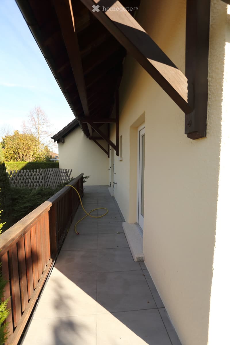 Balcony / Terrace. A balcony with a wooden railing and tiled floor, connected to a house with a white door.