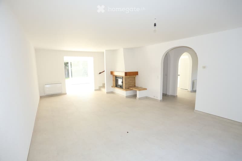 Unfurnished Room. Empty room with white walls, tiled floor, and a fireplace with a wooden mantle. There are two doors, one leading to a staircase and the other to another room.