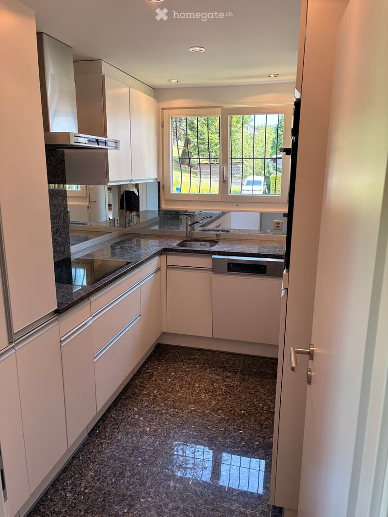 Modern kitchen with light-colored cabinets, granite countertops, and a stainless steel sink and dishwasher. The floor is tiled with dark granite tiles.