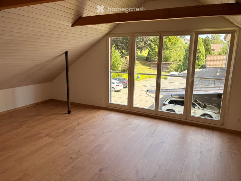 Empty attic room with wooden flooring, slanted wooden ceiling, large sliding glass doors leading to outdoor area.