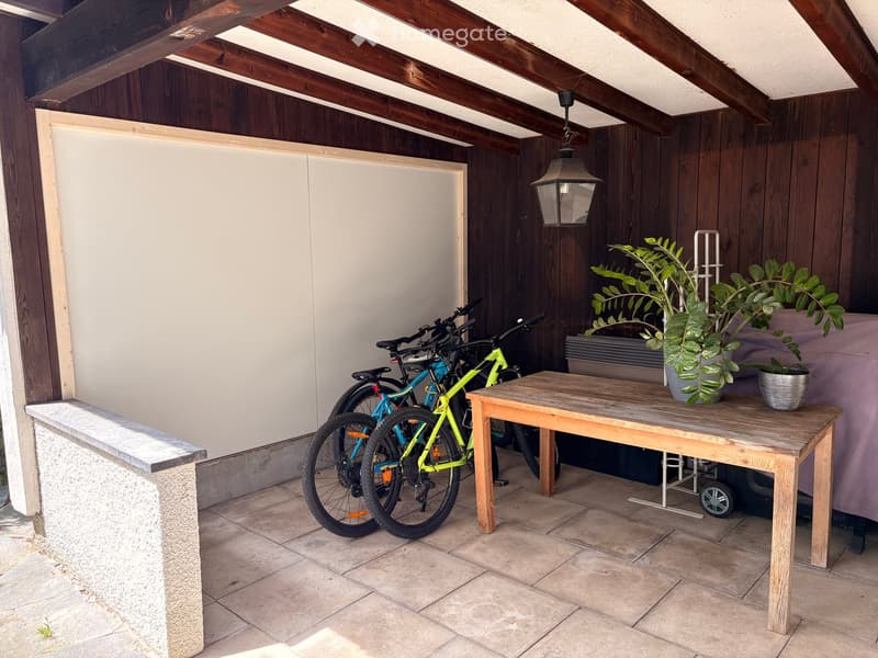Wooden table with potted plants, stone bench, and bicycles stored under a wooden pergola.