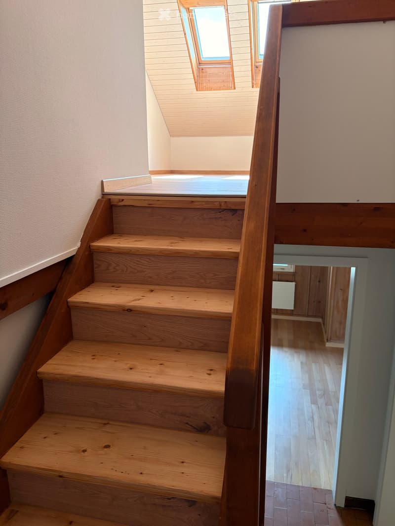 Wooden staircase with a handrail, leading to a room with wooden flooring and a visible doorway.
