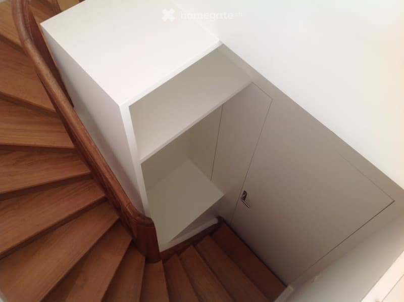 A modern staircase with wooden steps and a white wall-mounted cabinet. The staircase features a polished wooden handrail and a sleek, minimalist design.