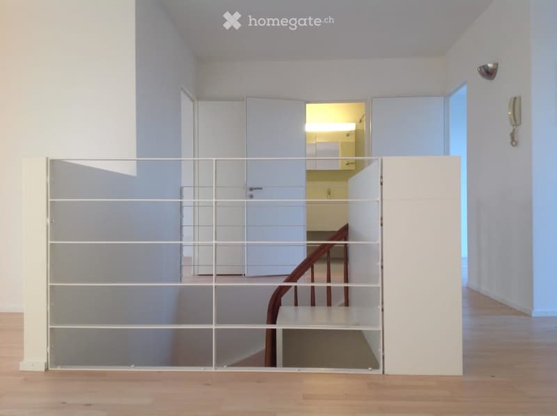 Modern hallway with white walls, wooden flooring, and a glass partition leading to a staircase and a room with cabinets.