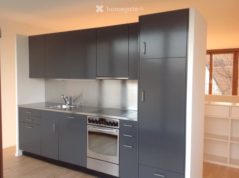 Modern kitchen with grey cabinets, stainless steel sink, and oven. Light wooden flooring and white walls.