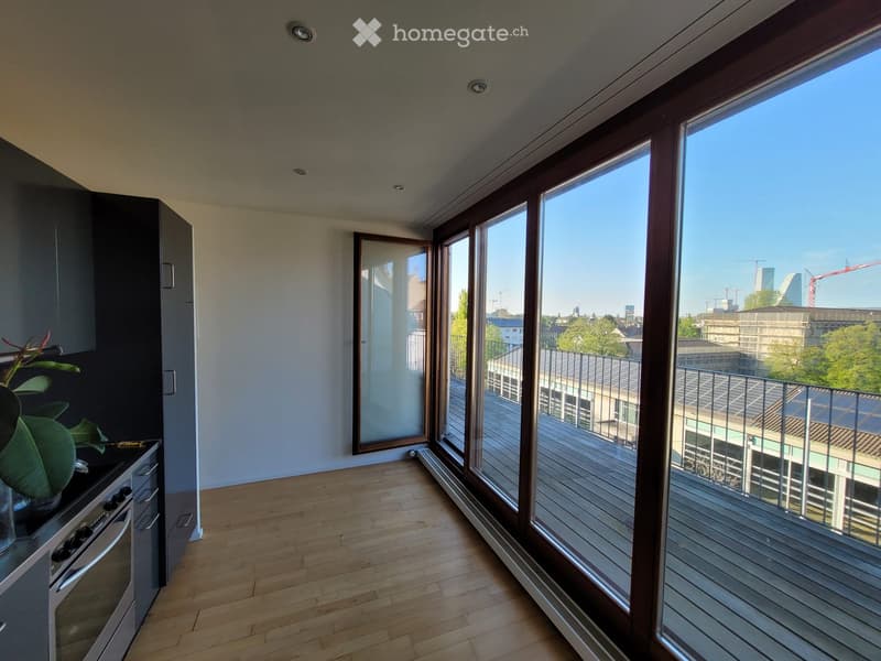 Modern kitchen with wooden flooring, large windows, and a balcony view of the city.
