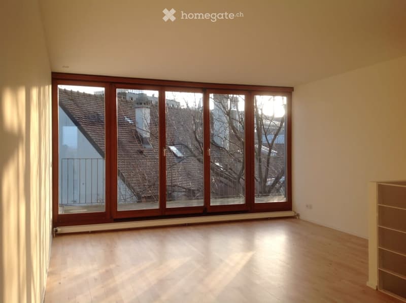 Empty room with wooden flooring and large sliding glass doors leading to a balcony. The walls are painted in a light color, and the space is well-lit with natural light.