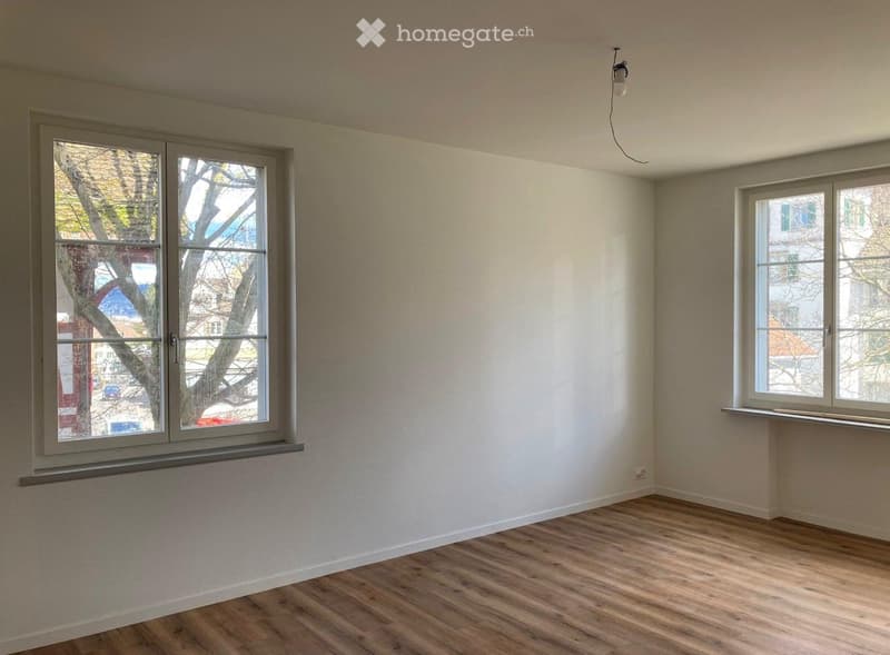 Empty room with wooden flooring, two windows, and white walls. No furniture or equipment present.