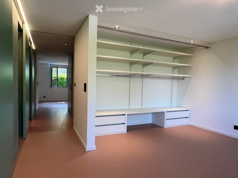 Empty room with built-in white shelving unit, drawers, and a window at the far end.