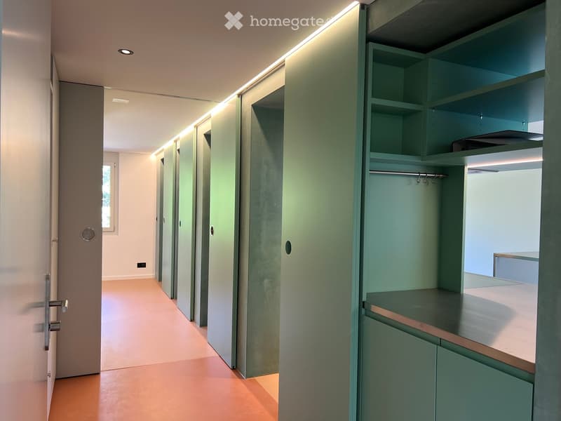Modern hallway with light green built-in storage units, recessed lighting, and a smooth wooden floor.