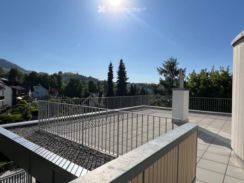 Balcony with metal railing, tiled floor, and a view of a residential area with trees and mountains in the background.