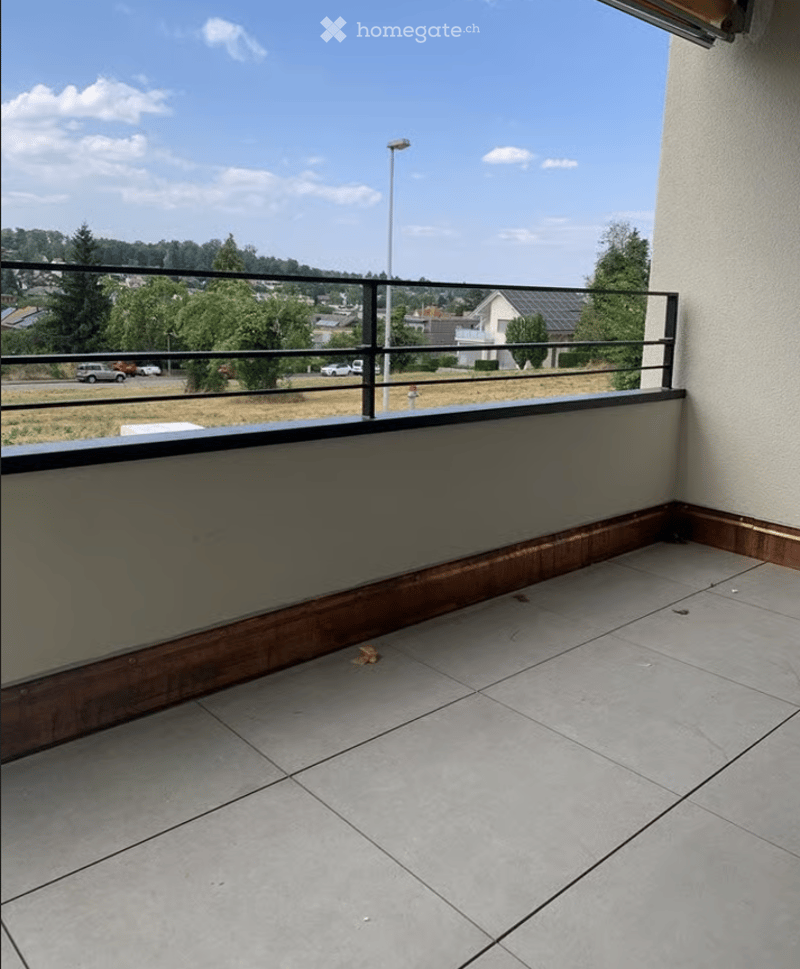 Balcony with tiled floor, wooden trim, metal railing, and a view of the surrounding area.