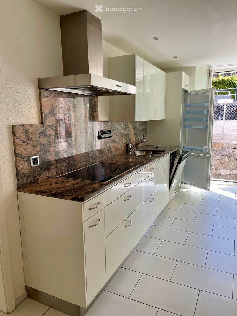 Modern kitchen with white cabinets, marble backsplash, and stainless steel appliances including a refrigerator, dishwasher, and range hood. The countertop features a sink and faucet.
