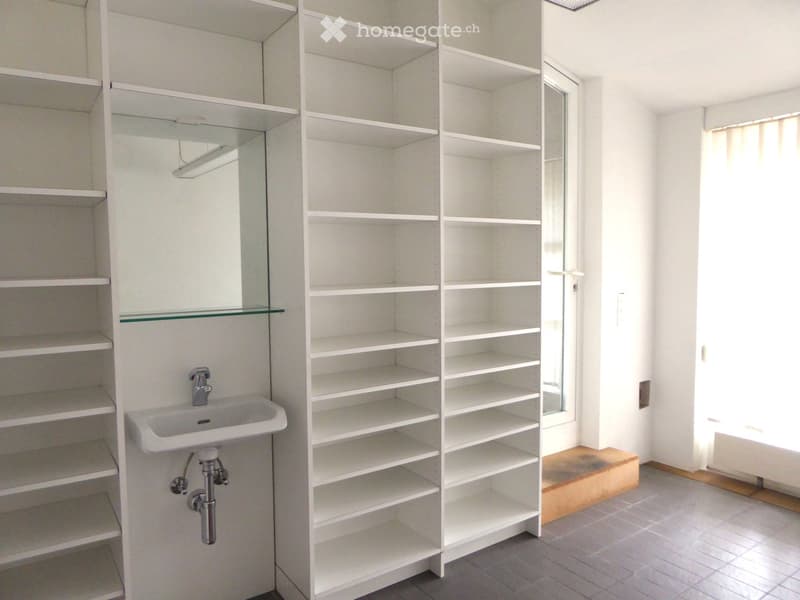 Modern bathroom with white tiled walls, a white sink with a chrome faucet, a large mirrored cabinet with glass shelves, and a window allowing natural light.