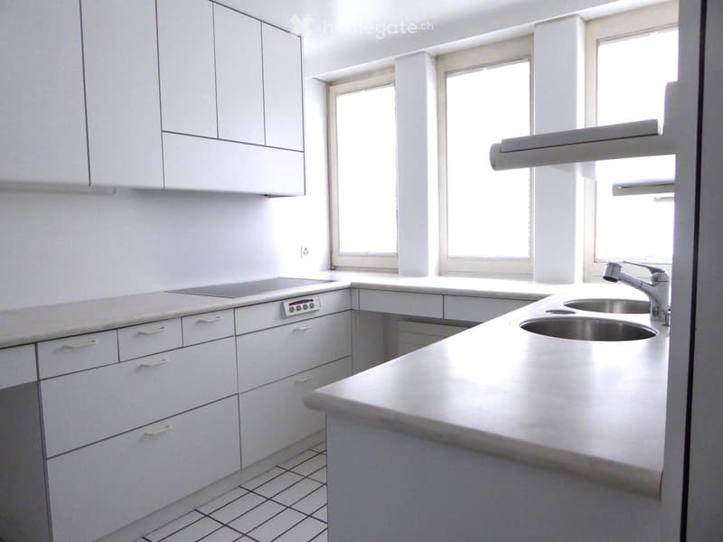 Modern kitchen with white cabinets, stainless steel sink, and countertop. Features large windows allowing natural light to fill the space.