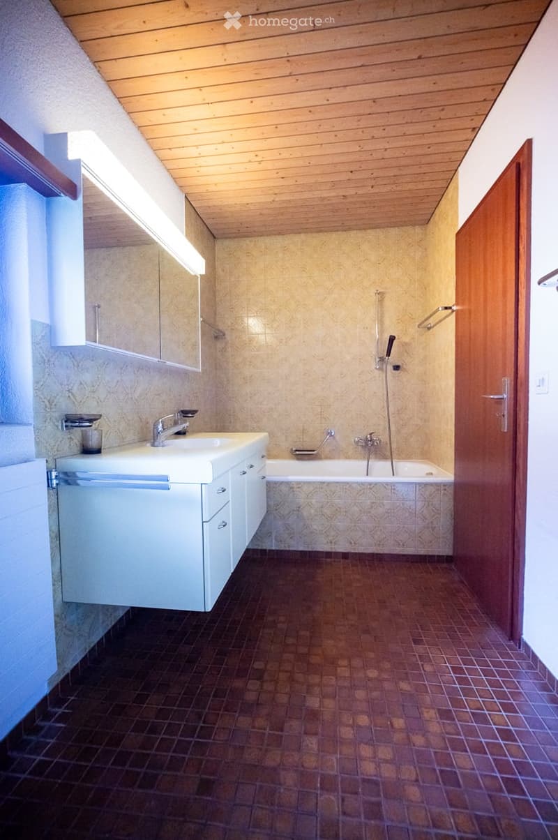 Bathroom with a wooden ceiling, tiled walls, a white sink with a faucet, a bathtub, a mirror, and a wooden door.