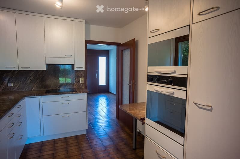 Modern kitchen with white cabinets, stainless steel oven, and granite countertops. The space features a tiled floor and an open doorway leading to another room.