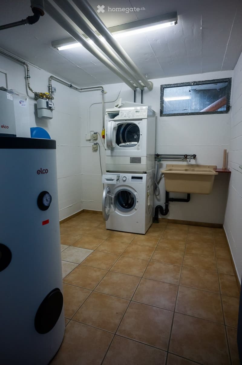 Utility room with a stacked washer and dryer, water heater, and sink.