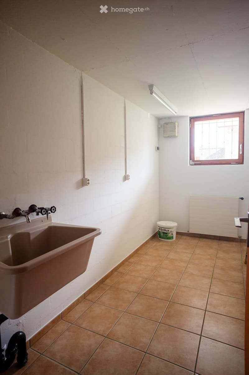 Empty room with tiled floor, white walls, a sink, a window, and a bucket on the floor.