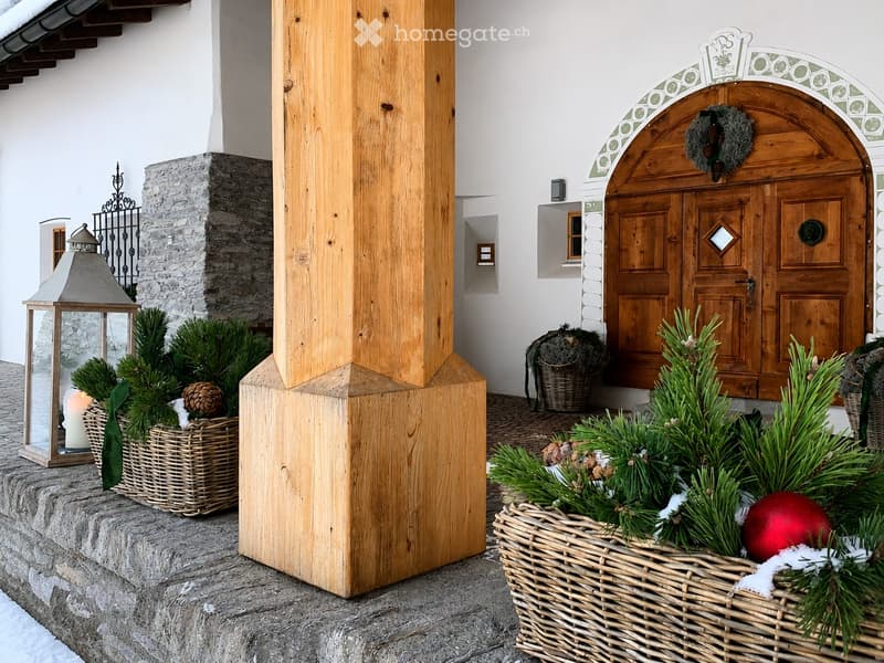 Entrance area with a wooden door, stone steps, wooden column, and festive wreaths and decorations in woven baskets.