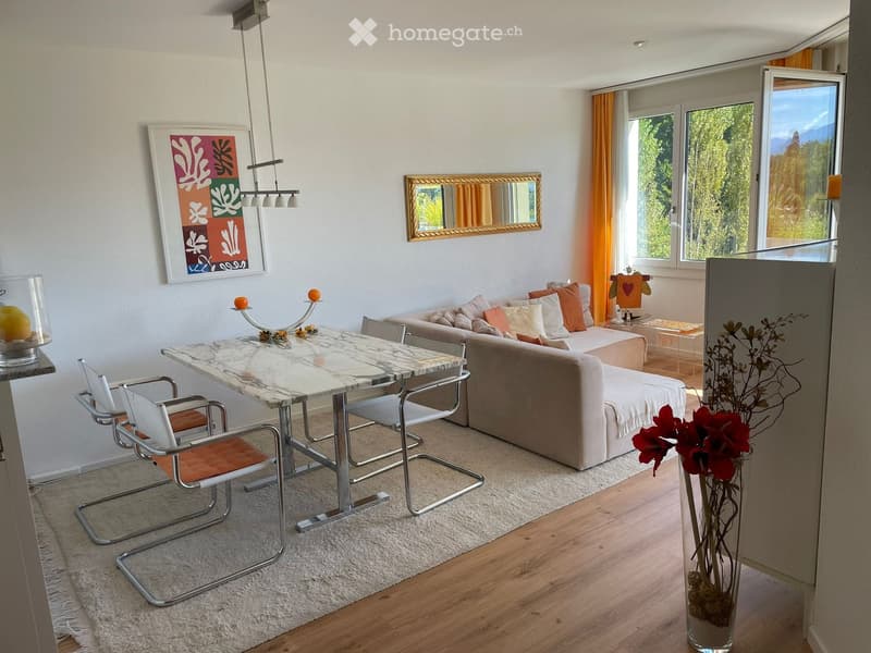 Modern living room with a beige sofa, white dining table with chairs, a vase with flowers, and a large window with orange curtains.