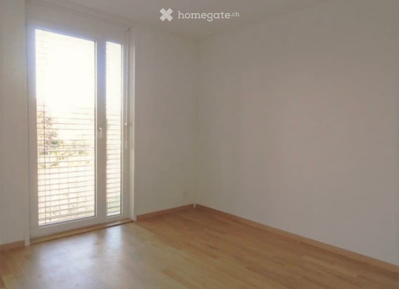 Empty room with wooden flooring, white walls, and large sliding glass door leading to a balcony.