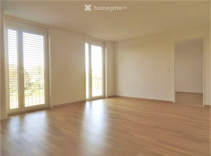 Empty room with wooden flooring, large sliding glass doors leading to a balcony, and white walls.